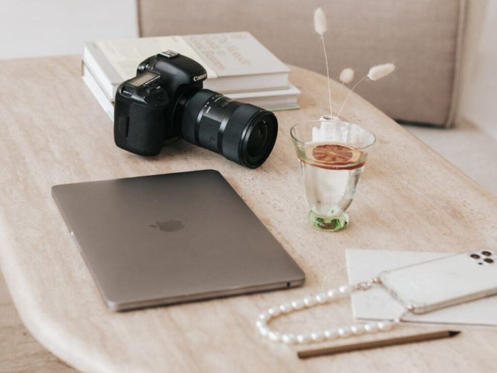 Macbook e Máquina Fotográfica numa mesa de madeira